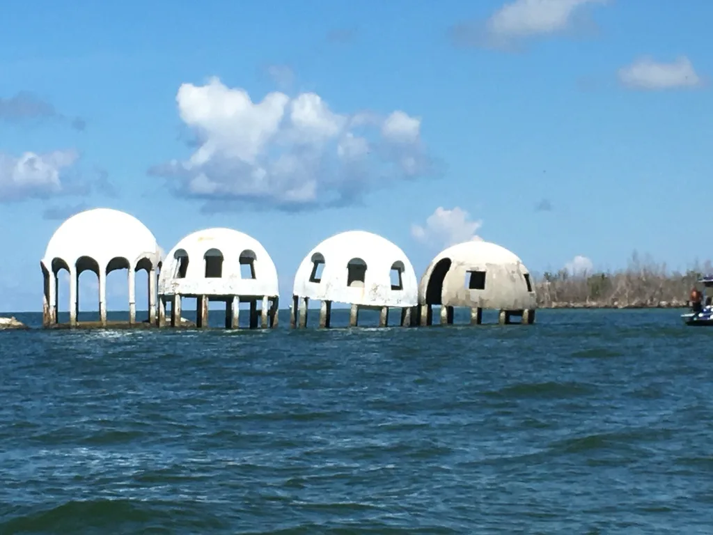 Abandoned dome houses standing in shallow water under a blue sky.