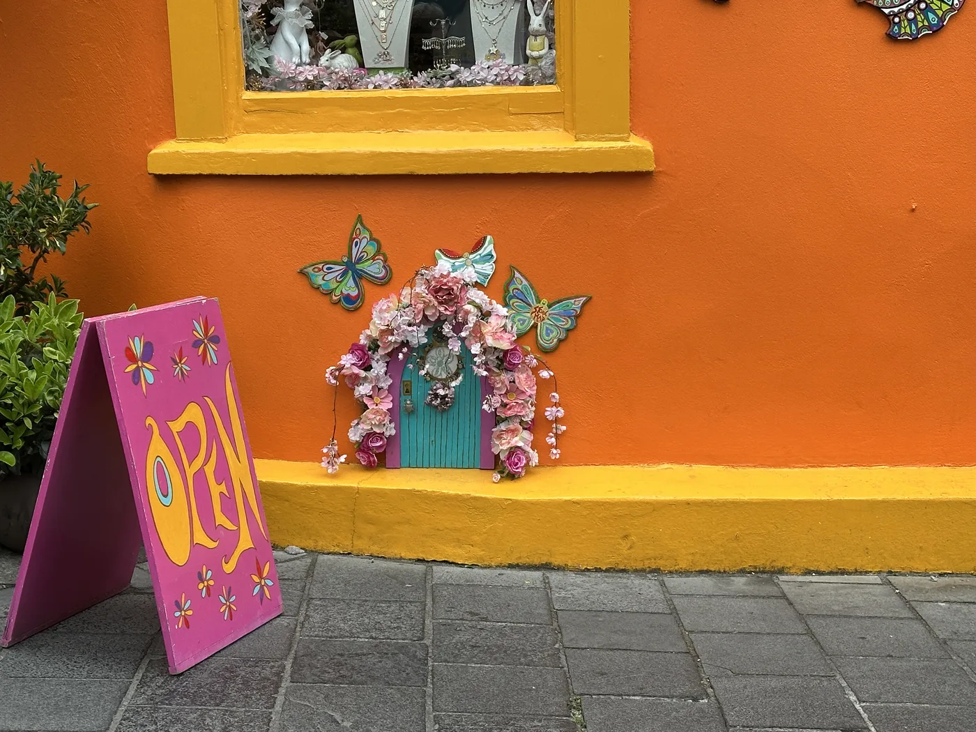 Fairy door framed by flowers on an orange Irish shopfront wall.